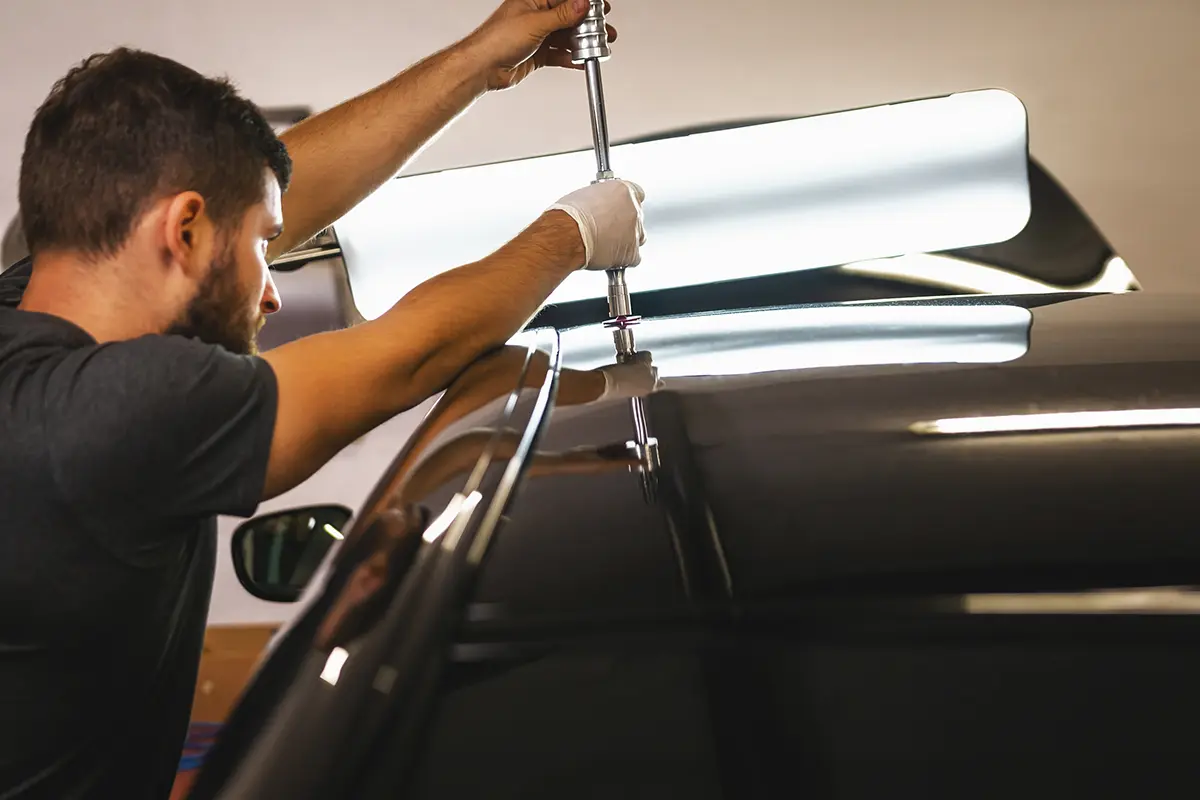 Technician performing hail damage repair on a vehicle in a professional repair facility.