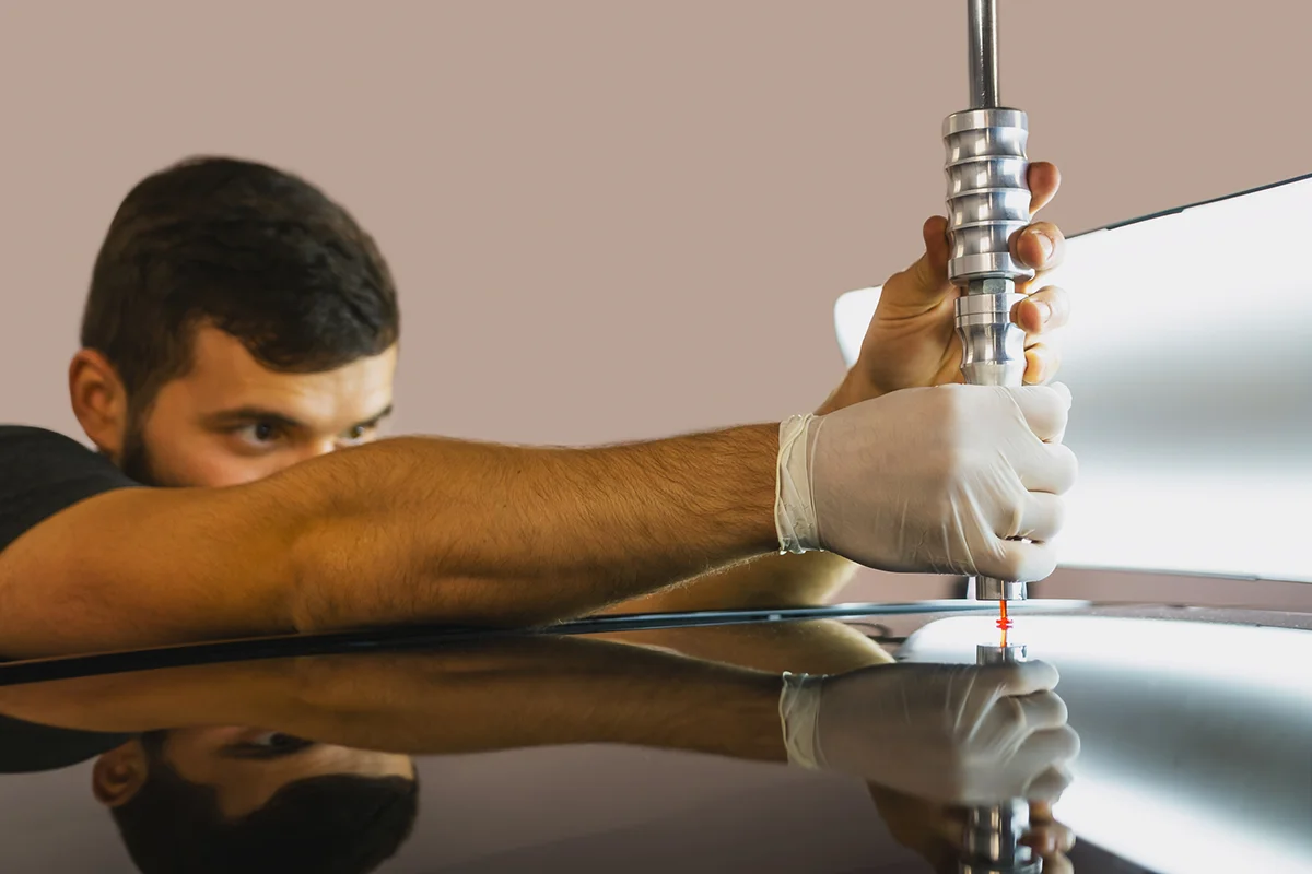 Paintless dent repair (PDR) technician using specialized tools to remove a dent from a vehicle's surface.