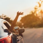 Car passenger enjoying the summer sun with hand waving out car window in breeze.