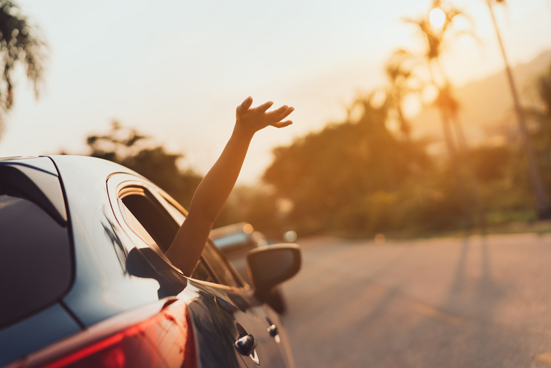 Car passenger enjoying the summer sun with hand waving out car window in breeze.