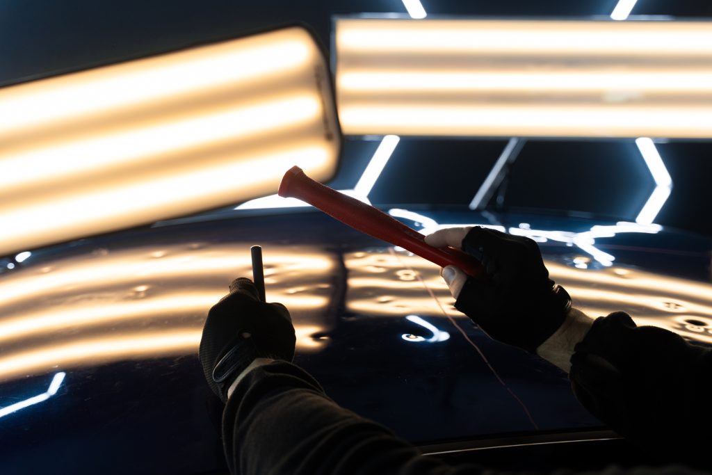 Dent repair technician using special tools and lighting.
